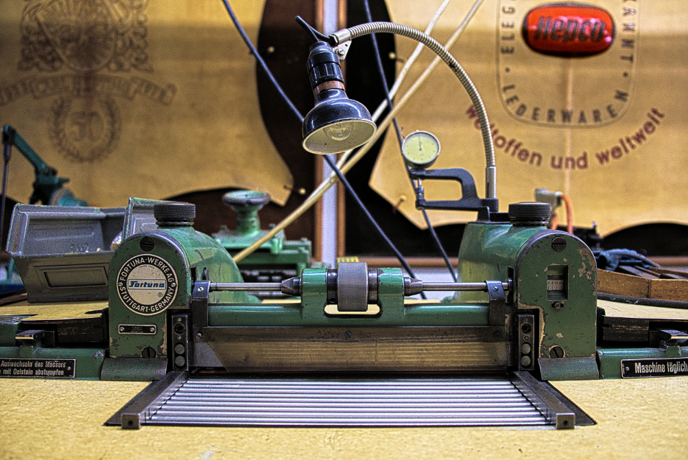 Eine Ausschärfmaschine der Marke Fortuna steht neben anderen Maschinen in einer Manufaktur. Im Hintergrund hängen historische Dekorationshäute der Hepco Manufaktur