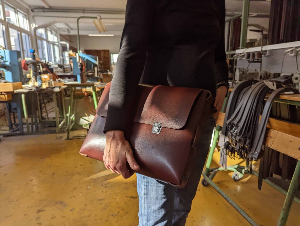 Eine Frau präsentiert die Tasche Blyss von Hepco in der Hepco Manufaktur in der nähe von Stuttgart. Sie hält sie in das Sonnenlicht. Die Tasche ist braun.